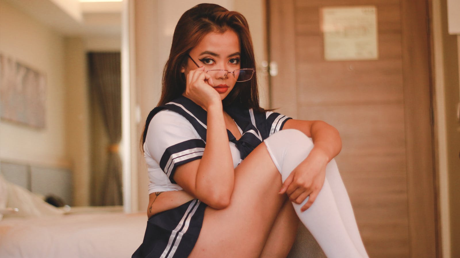 Model posing in a stylish school uniform cosplay indoors, showcasing fashion elegance.